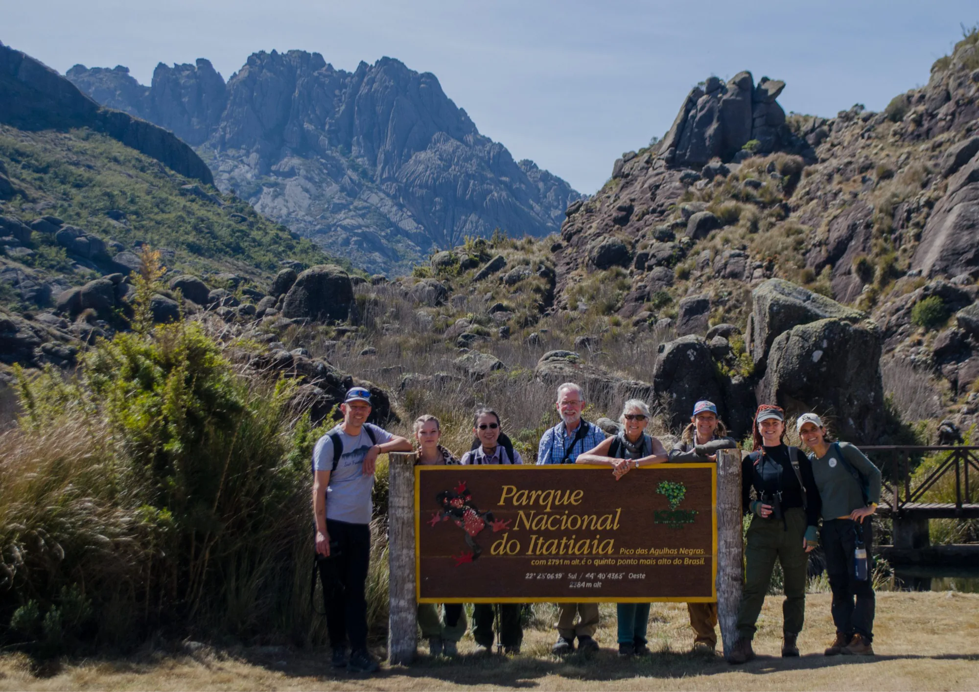 Grupo posando junto à placa do Parque Nacional do Itatiaia, com o Pico das Agulhas Negras ao fundo