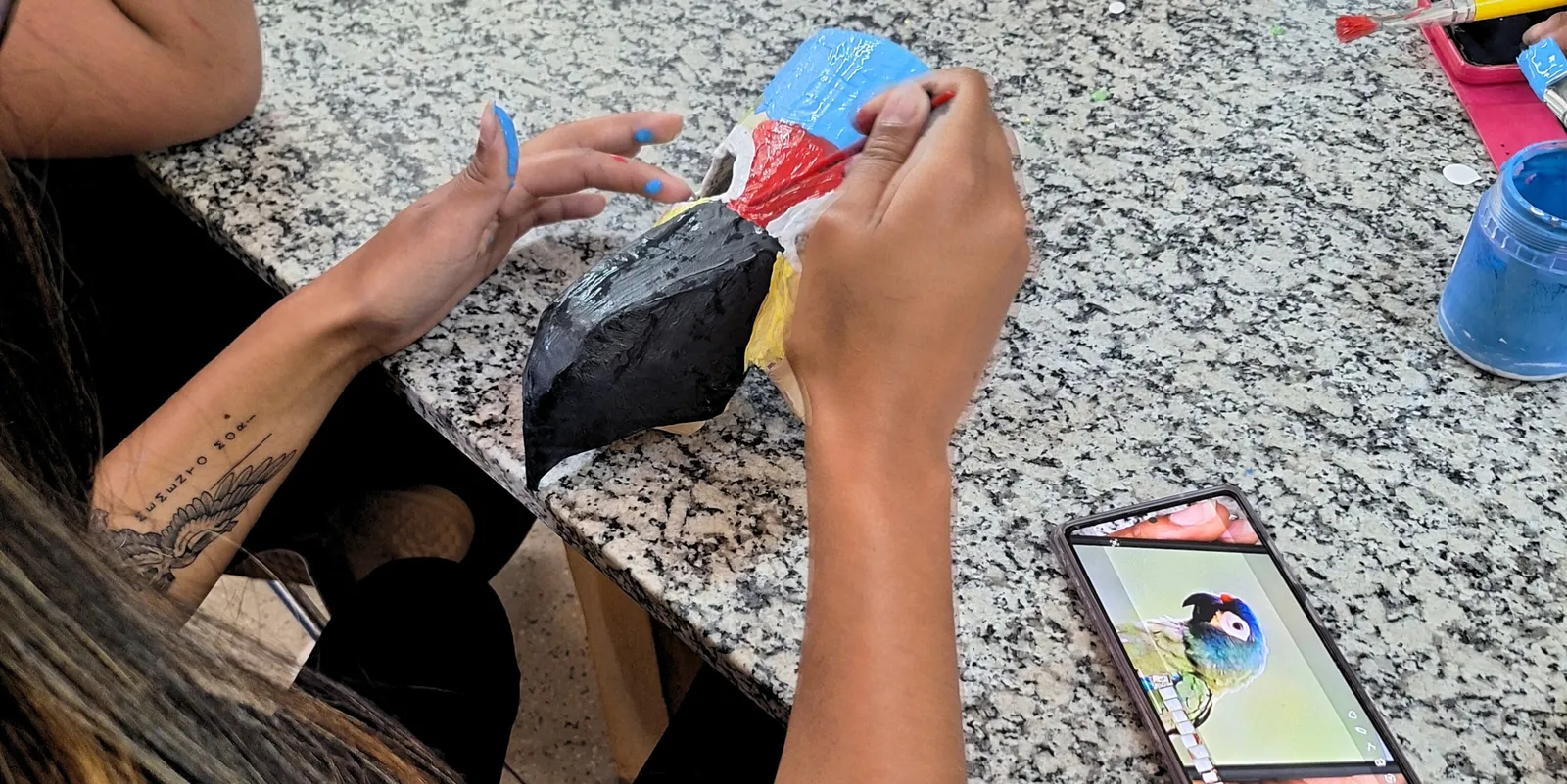 Participante pintando uma máscara de ave em papel machê durante oficina de artes