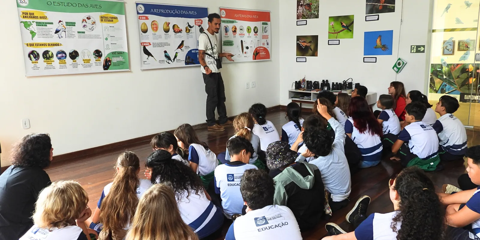 Educador do OAMa apresentando painéis sobre estudo de aves para estudantes sentados no chão